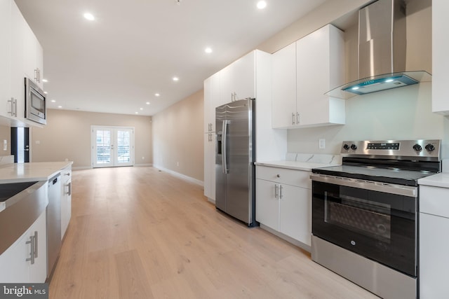 kitchen featuring french doors, light wood-style floors, white cabinetry, wall chimney range hood, and appliances with stainless steel finishes