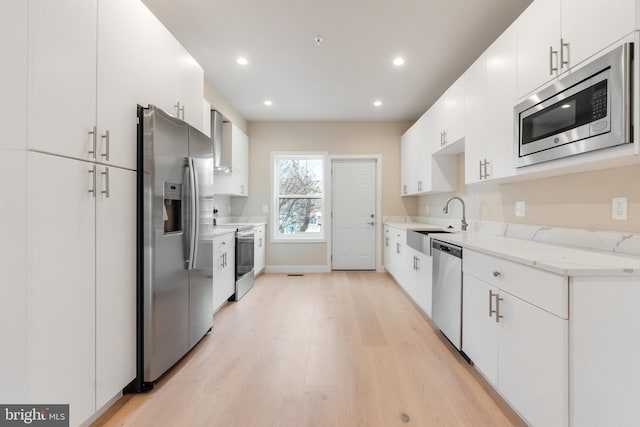 kitchen with recessed lighting, a sink, wall chimney exhaust hood, stainless steel appliances, and light wood-type flooring