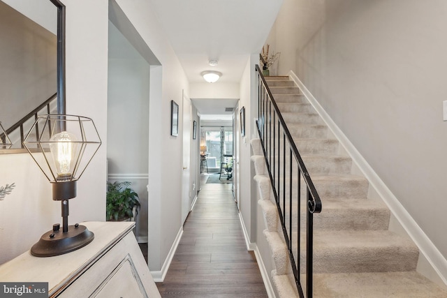hallway with dark wood-style flooring, stairs, and baseboards