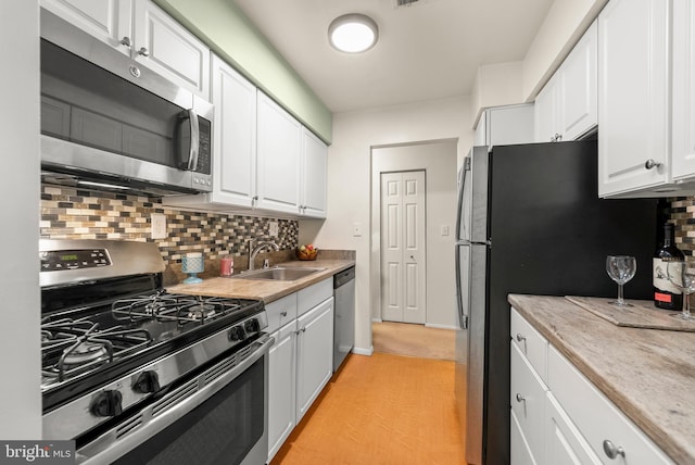 kitchen with appliances with stainless steel finishes, a sink, white cabinets, decorative backsplash, and light countertops