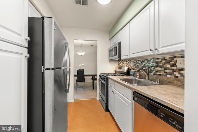 kitchen featuring appliances with stainless steel finishes, a sink, white cabinets, tasteful backsplash, and light countertops