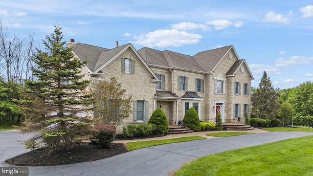 view of front of property featuring brick siding, a chimney, and a front yard