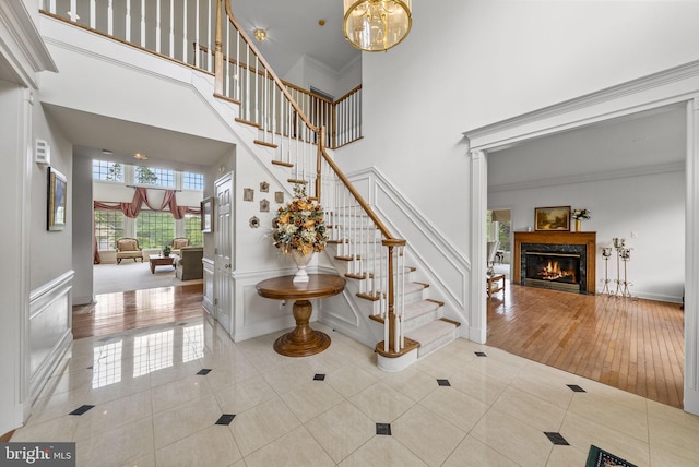 entryway featuring a towering ceiling, stairway, tile patterned floors, a glass covered fireplace, and a chandelier