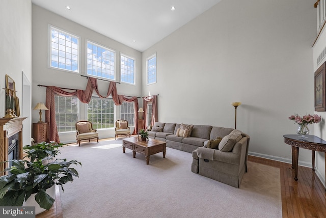 living room featuring a towering ceiling, a high end fireplace, wood finished floors, baseboards, and recessed lighting