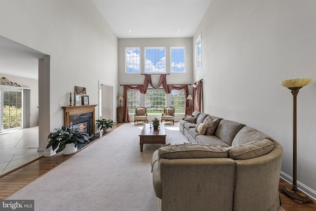 living room with a premium fireplace, a towering ceiling, baseboards, and wood finished floors