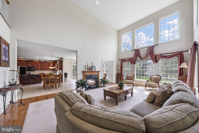 living room with high vaulted ceiling, light wood-type flooring, healthy amount of natural light, a premium fireplace, and recessed lighting