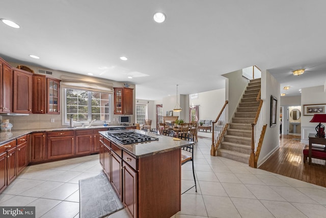 kitchen featuring gas stovetop, a kitchen breakfast bar, a kitchen island, glass insert cabinets, and recessed lighting