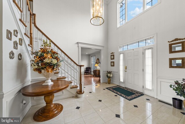 foyer with stairs, a decorative wall, a chandelier, a high ceiling, and wainscoting