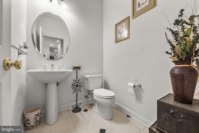 half bathroom featuring toilet, tile patterned flooring, baseboards, and a sink