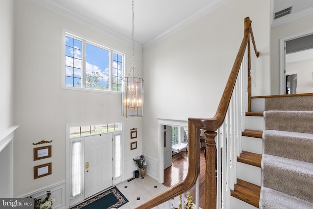 foyer entrance featuring stairway, ornamental molding, a chandelier, and a towering ceiling
