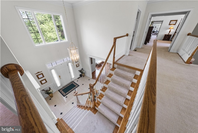 stairway featuring a high ceiling, baseboards, a chandelier, carpet flooring, and crown molding