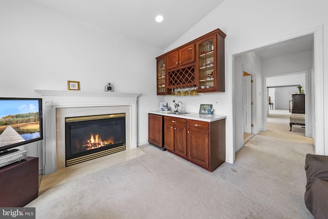 indoor wet bar featuring light colored carpet, lofted ceiling, and a fireplace with flush hearth