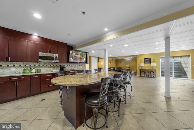 kitchen featuring stainless steel microwave, light tile patterned floors, decorative backsplash, recessed lighting, and a kitchen bar