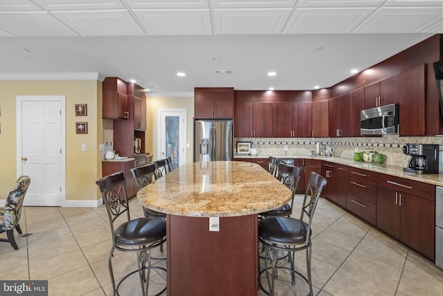 kitchen with appliances with stainless steel finishes, dark brown cabinets, decorative backsplash, a center island, and crown molding