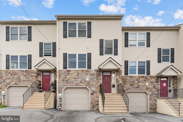 multi unit property featuring an attached garage, stone siding, and driveway