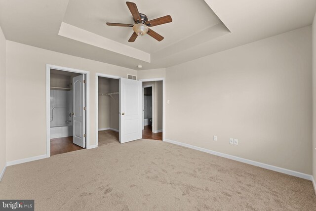 unfurnished bedroom featuring carpet floors, a tray ceiling, baseboards, ensuite bath, and a closet