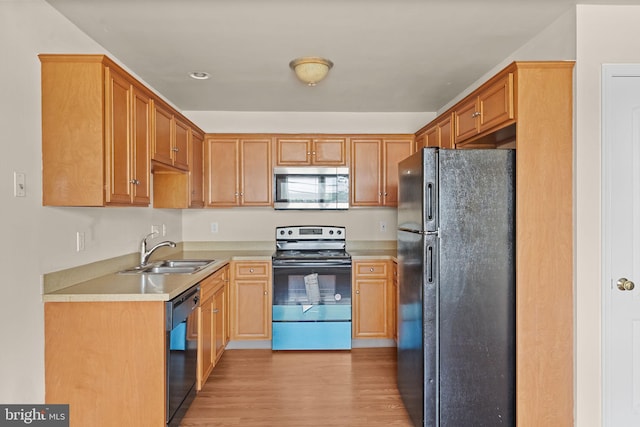 kitchen featuring black appliances, a sink, light wood-style floors, and light countertops