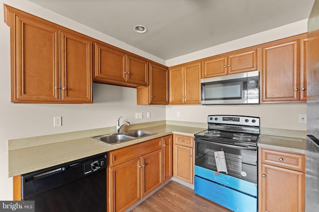 kitchen with appliances with stainless steel finishes, a sink, light wood finished floors, and light countertops