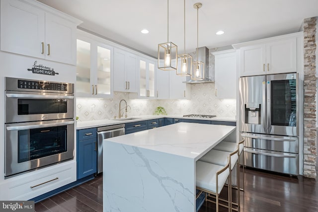 19599 Aspendale Sq, Ashburn, VA 20147 - kitchen featuring stainless steel appliances, blue cabinets, wall chimney range hood, a sink, and dark wood-type flooring