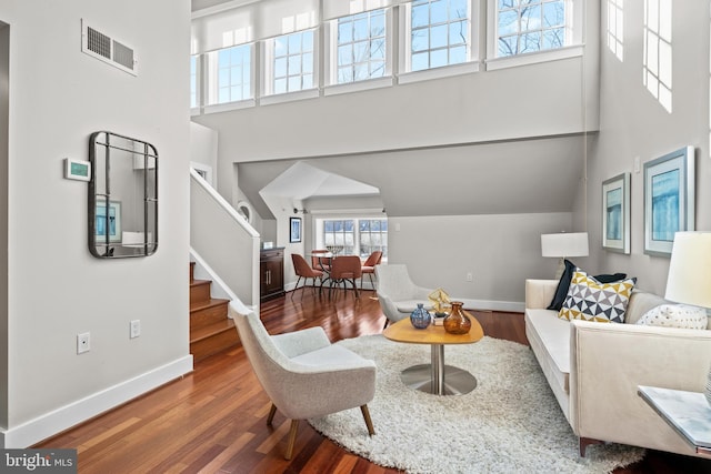 living room with wood finished floors, a towering ceiling, visible vents, stairway, and baseboards