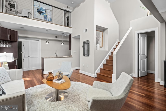 living area with stairs, baseboards, visible vents, and dark wood finished floors