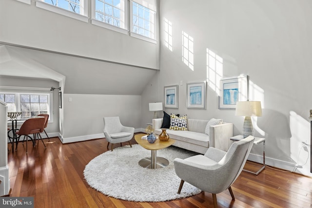 living room featuring a high ceiling, baseboards, and hardwood / wood-style floors