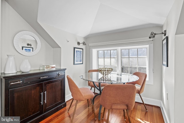 dining room featuring baseboards, wood-type flooring, and vaulted ceiling