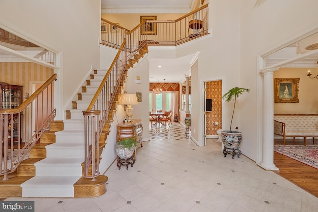 tiled foyer with stairs, ornate columns, a chandelier, and a towering ceiling