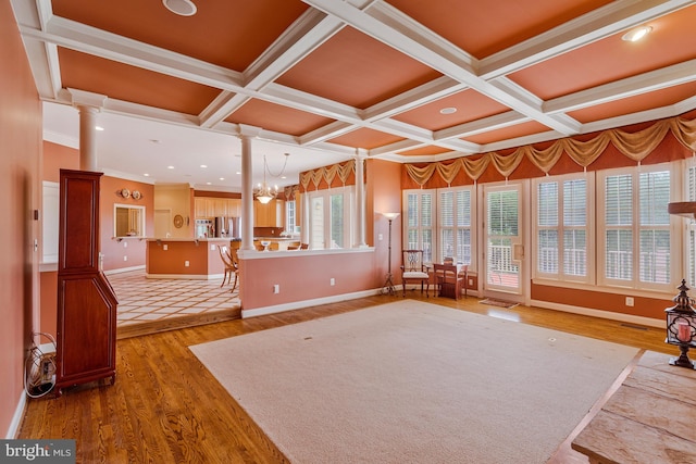 unfurnished living room with wood finished floors, coffered ceiling, decorative columns, crown molding, and baseboards