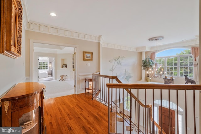 hall featuring light wood finished floors, an upstairs landing, crown molding, and a wealth of natural light