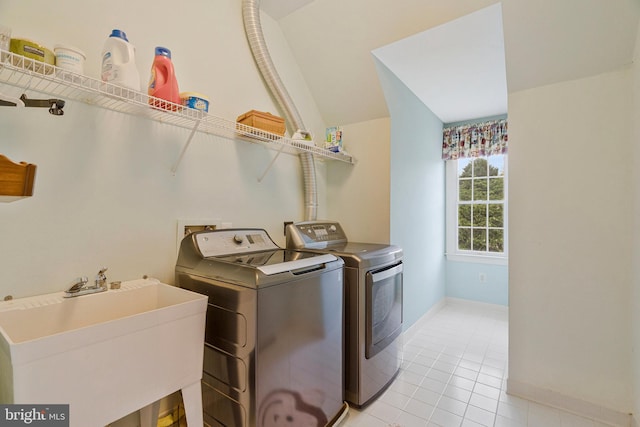 washroom with baseboards, light tile patterned floors, washer and dryer, a sink, and laundry area
