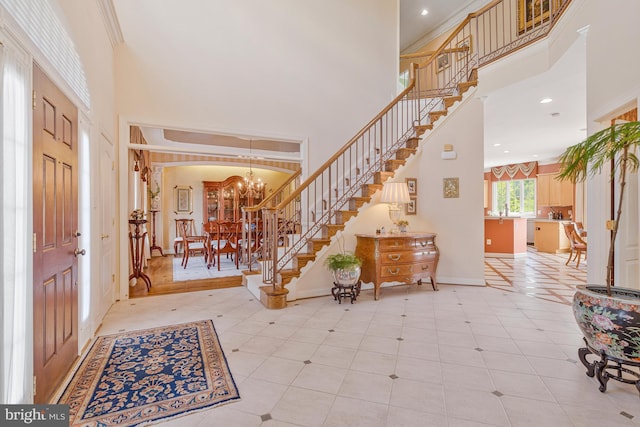 foyer featuring a towering ceiling, stairway, an inviting chandelier, light tile patterned floors, and baseboards