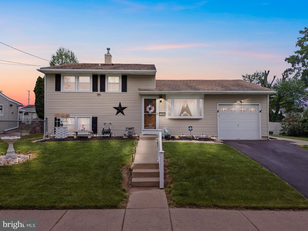 split level home with a chimney, fence, a garage, a front yard, and aphalt driveway