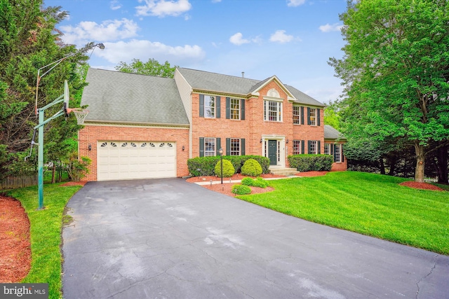colonial-style house featuring asphalt driveway, an attached garage, a front yard, and brick siding