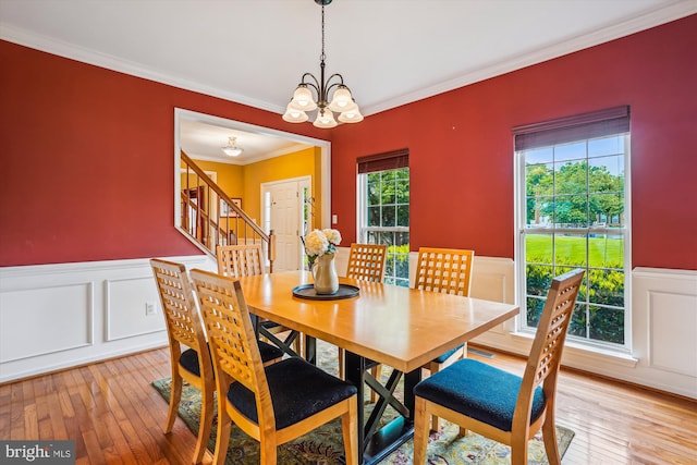 dining space featuring crown molding, a wainscoted wall, a chandelier, a decorative wall, and stairway