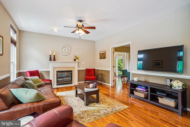 living area featuring ceiling fan, wood finished floors, and a fireplace with flush hearth