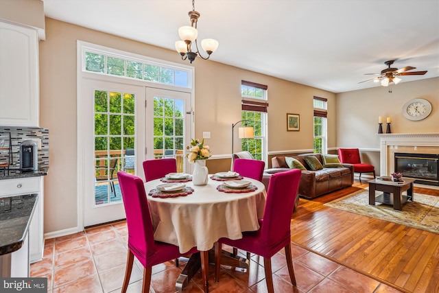 dining room featuring a ceiling fan, light tile patterned floors, a chandelier, and a glass covered fireplace