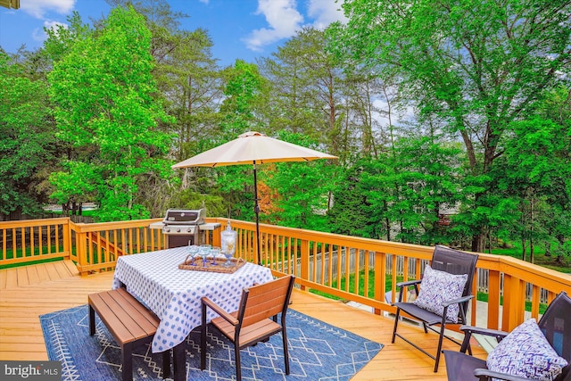 deck featuring area for grilling, outdoor dining space, and view of wooded area