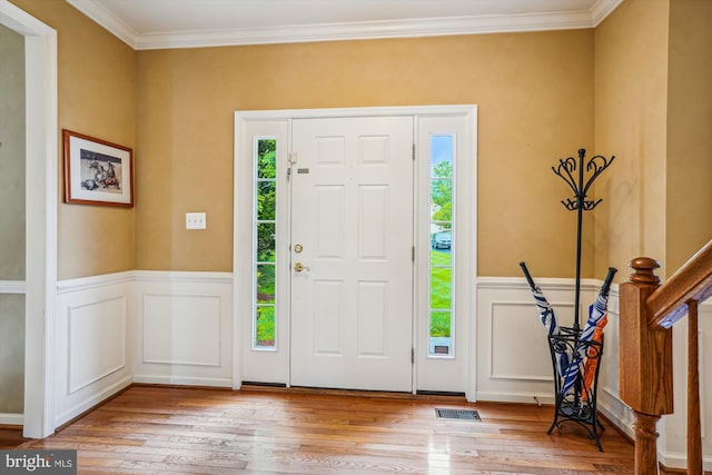 entryway with light wood finished floors, crown molding, a wainscoted wall, and a decorative wall