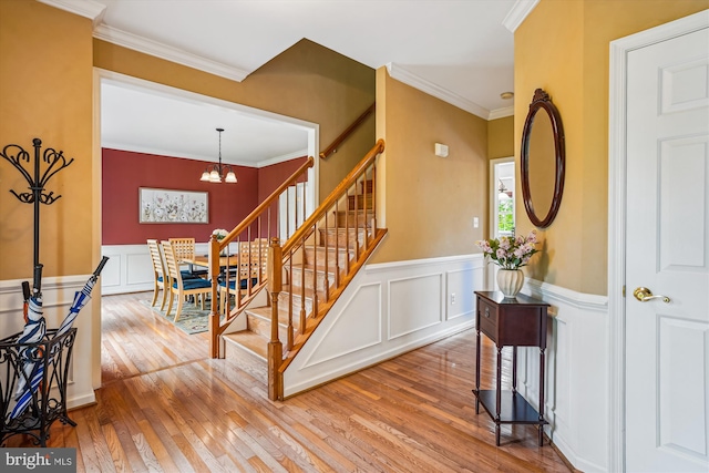 stairs with hardwood / wood-style floors, a chandelier, wainscoting, ornamental molding, and a decorative wall