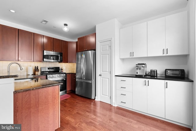 kitchen with appliances with stainless steel finishes, a sink, wood finished floors, recessed lighting, and tasteful backsplash