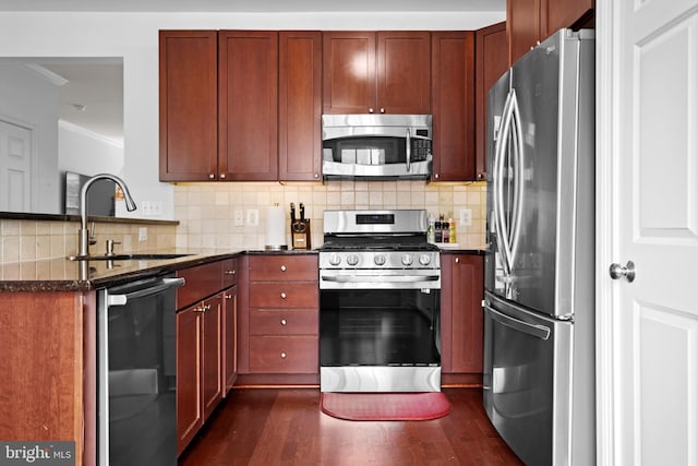 kitchen featuring stainless steel appliances, a sink, a peninsula, dark wood-style floors, and backsplash