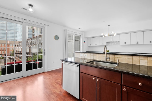 kitchen with a sink, dishwasher, decorative backsplash, wood finished floors, and a chandelier
