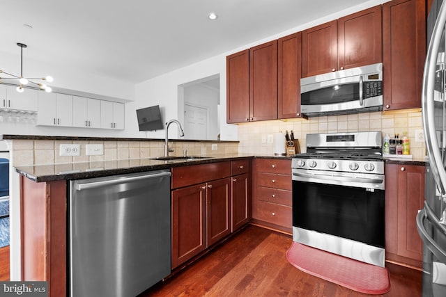kitchen with stainless steel appliances, a sink, dark wood-style floors, tasteful backsplash, and dark stone countertops