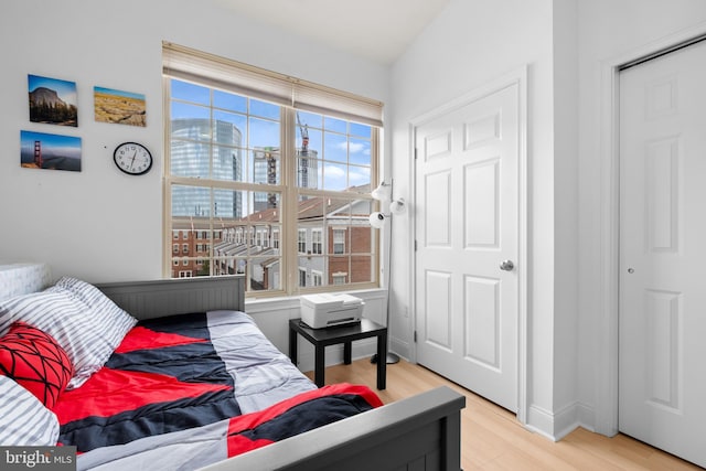 bedroom featuring light wood finished floors, a view of city, and baseboards