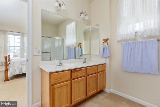 full bathroom with double vanity, a sink, a shower with shower door, baseboards, and ensuite bath