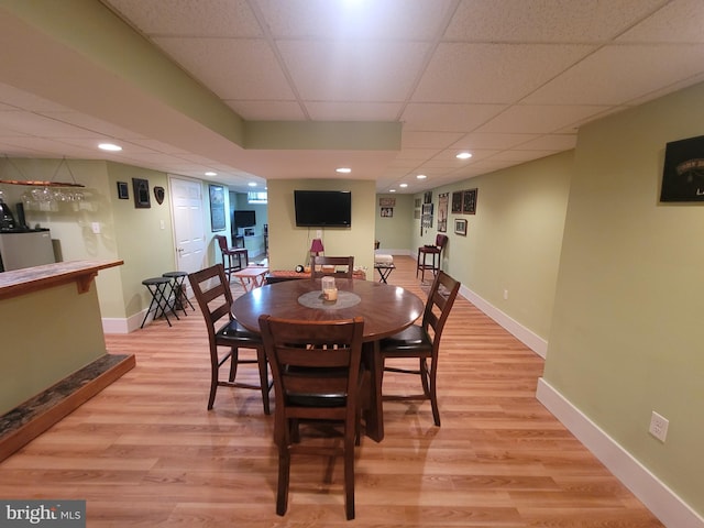 dining room with a paneled ceiling, baseboards, light wood finished floors, and bar