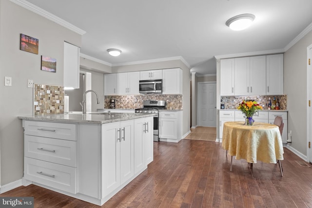 kitchen featuring stainless steel appliances, a sink, tasteful backsplash, white cabinets, and ornamental molding
