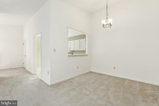spare room with a chandelier, light colored carpet, and baseboards