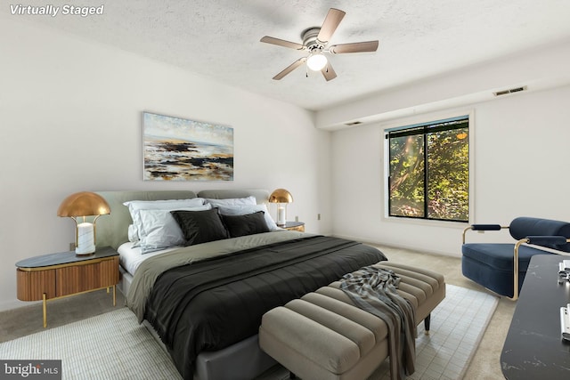 bedroom featuring light colored carpet, a textured ceiling, and ceiling fan